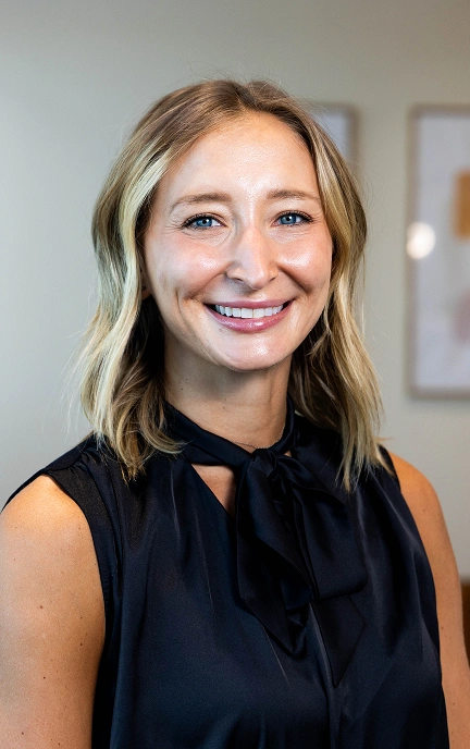 Professional woman smiling at camera in dental office setting, wearing black sleeveless top.