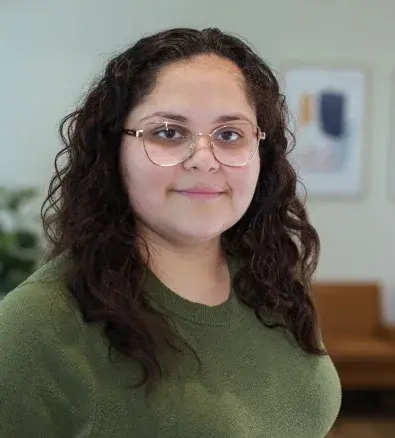 Young woman with curly dark hair and glasses smiling at Peoria dental practice.